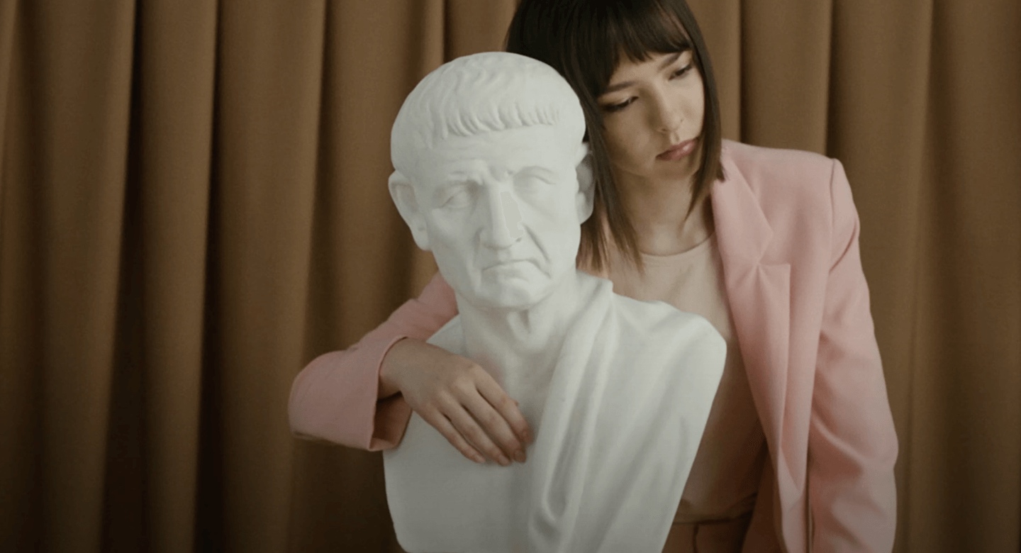 A woman in a pink jacket hugging the statue of an ancient greek